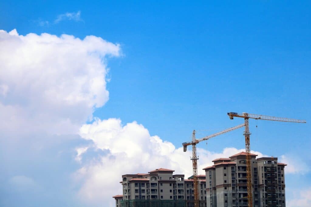 Crane Construction At High-Rise Building Site Under Blue Sky With Clouds.