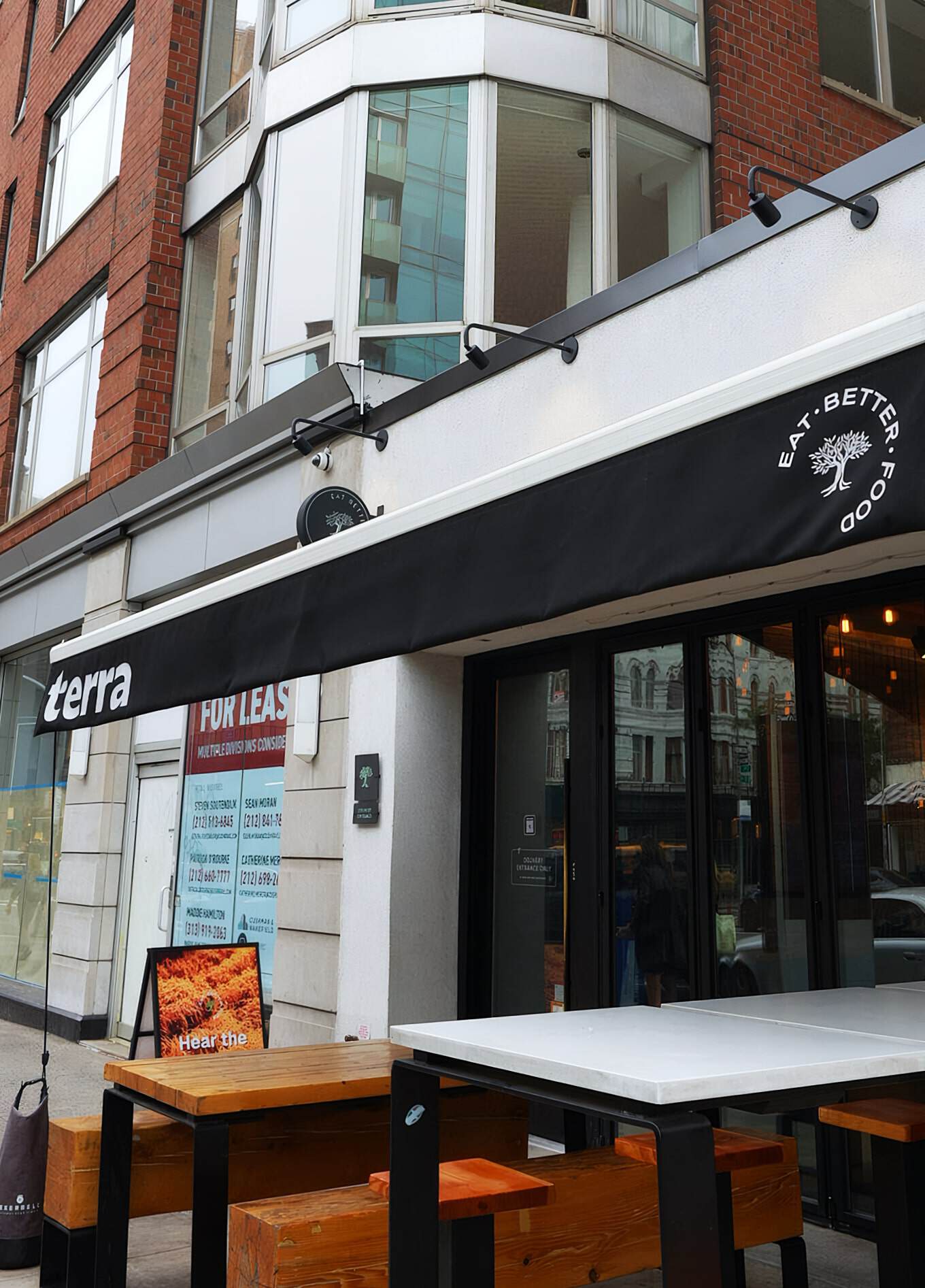 Modern Urban Restaurant Building With Large Windows, Outdoor Seating Area, And Black Awning Featuring The 